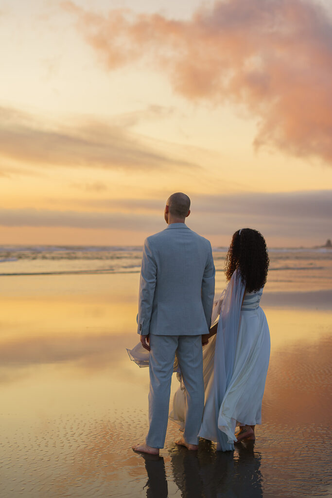 Couple stares out to the sunset while standing on the shore during their Cannon Beach bridal portraits.