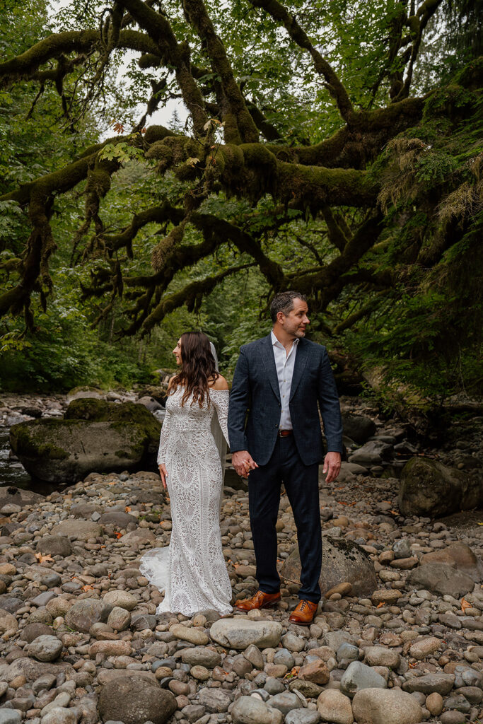 Couple stands and poses near a river bend in a mossy forest in Washington