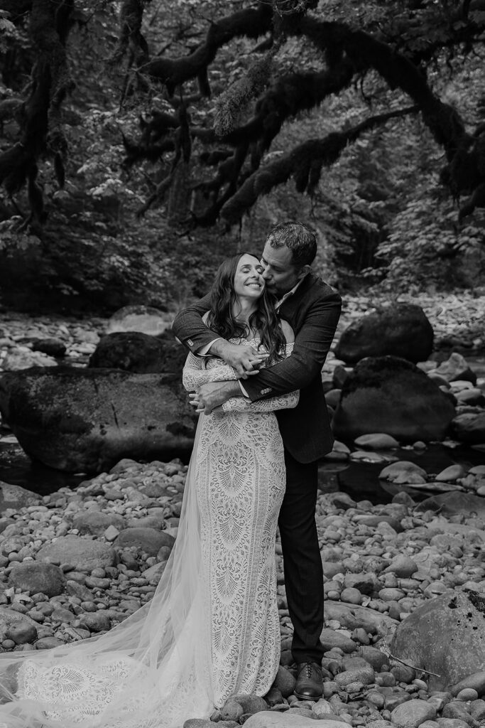 Couple stands and poses near a river bend in a mossy forest in Washington