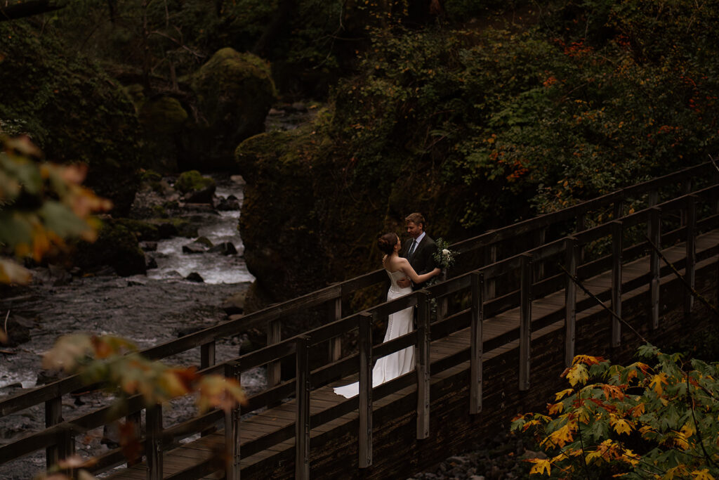 Bride and groom stand on a bridge near Wahclella Falls during their moody elopement