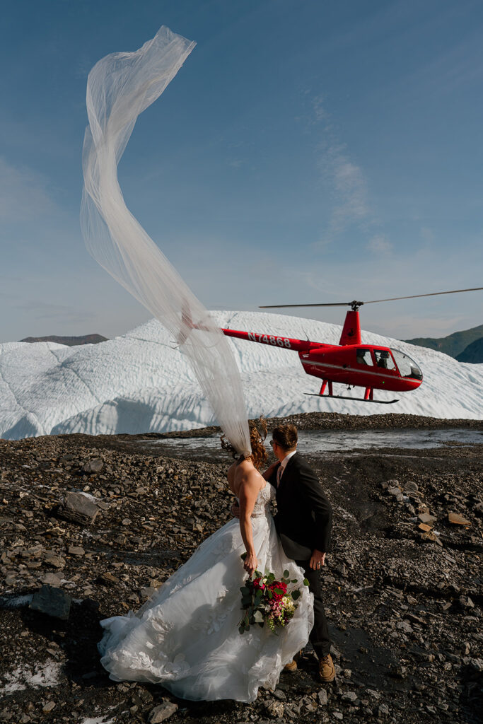 Bride and groom watch their helicopter land to pick them up for their glacier elopement