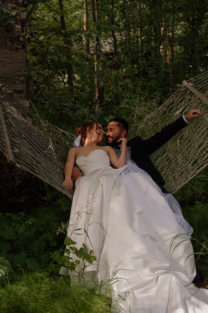 Bride and groom sit on a hammock in the woods