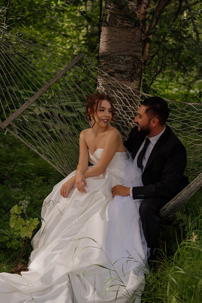 Bride and groom sit on a hammock in the woods