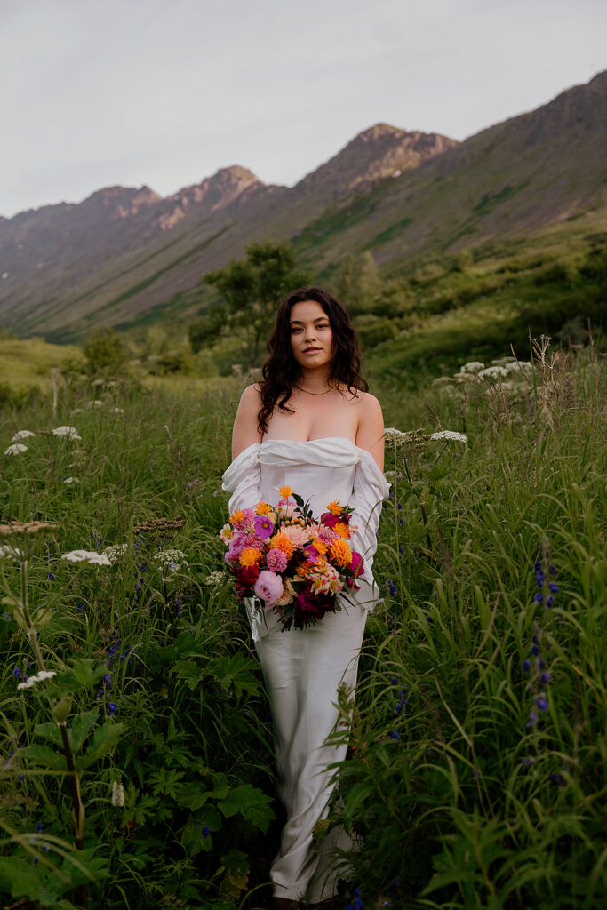 Bride walking through wildflowers with mountains in the background during an Anchorage Alaska elopement