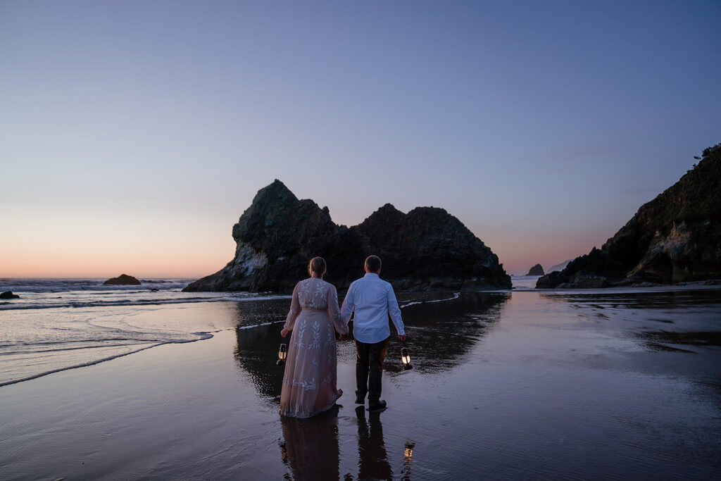 Couple walks with lanterns on Arcadia Beach, Oregon Coast at blue hour
