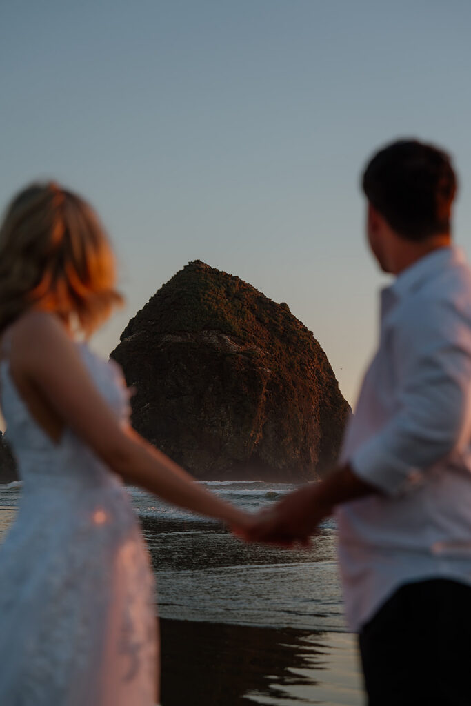 Couple stands at sunset looking at Haystack Rock on Cannon Beach on the Oregon Coast