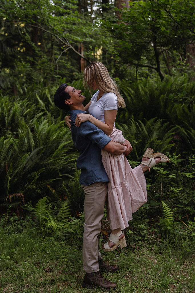 Couple stands in front of fern in a Washington forest during their lake engagement photos