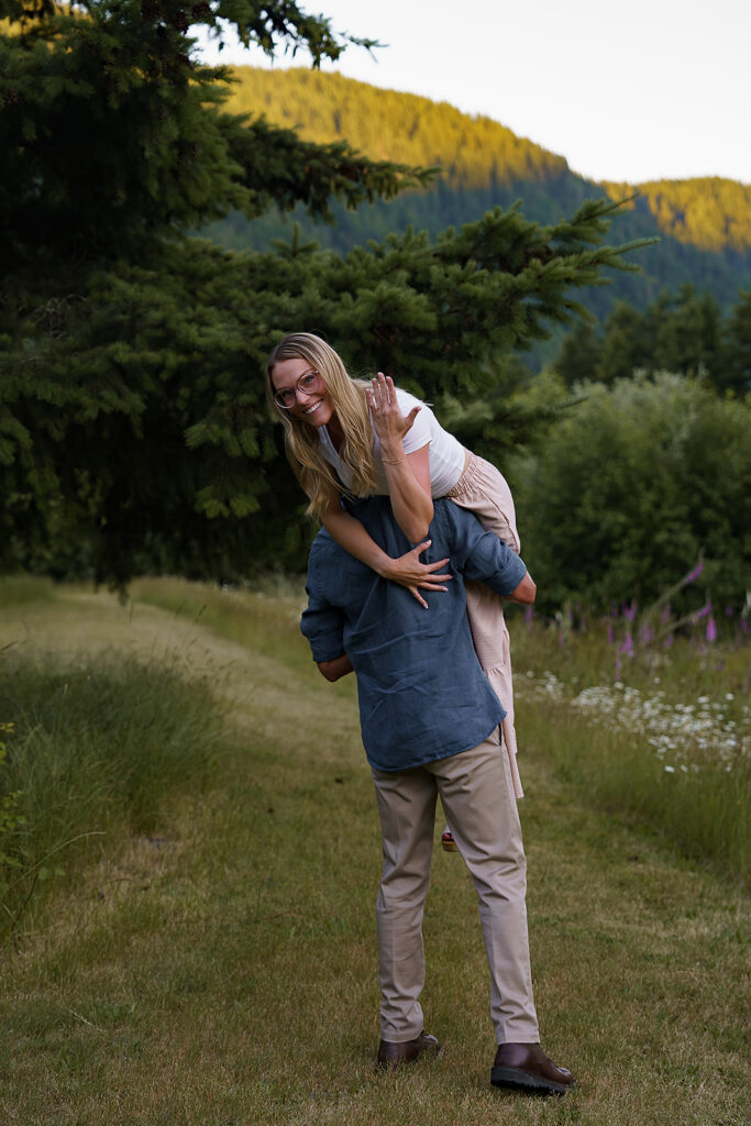 Man holds woman over his shoulder as she shows off her engagement ring