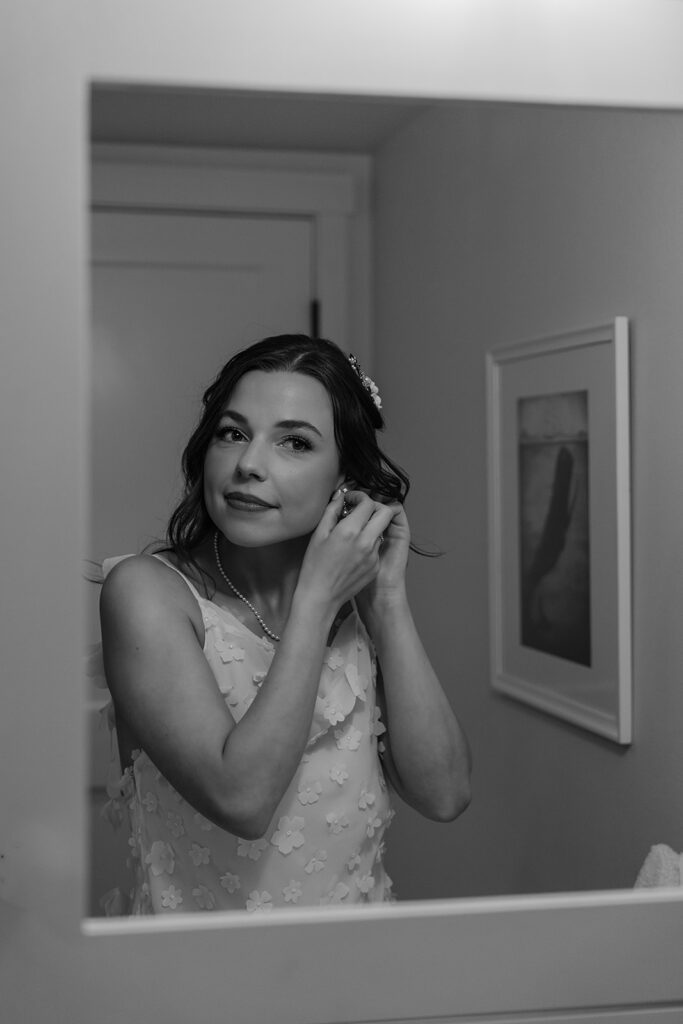 Bride puts in her earrings in the mirror