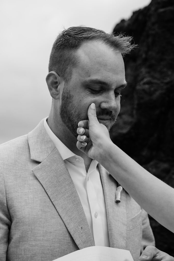 Bride wipes away a tear falling from groom's eye as he reads his vows on Arcadia Beach