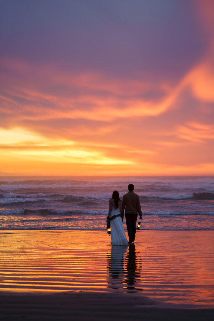 Bride and groom walk with lanterns at blue hour on the Oregon Coast