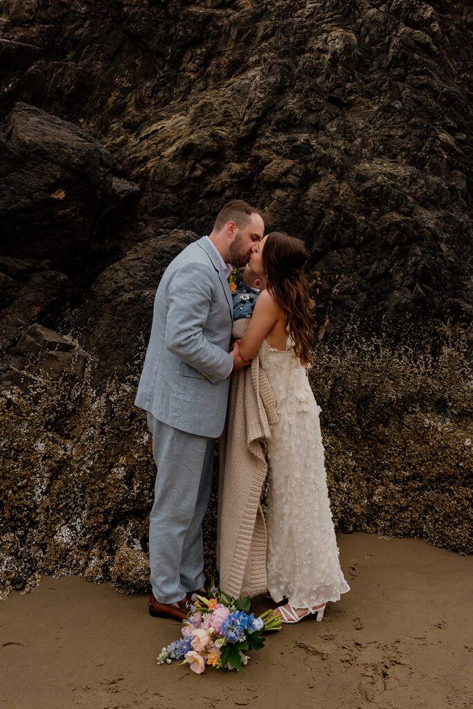 Bride and groom kiss after their Cannon Beach wedding ceremony as they hold their baby