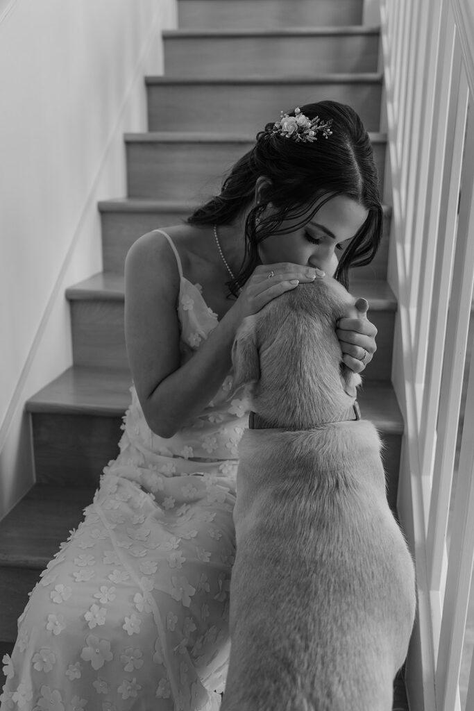Bride sits on a staircase in the Airbnb as she kisses her dog before a Cannon Beach wedding ceremony